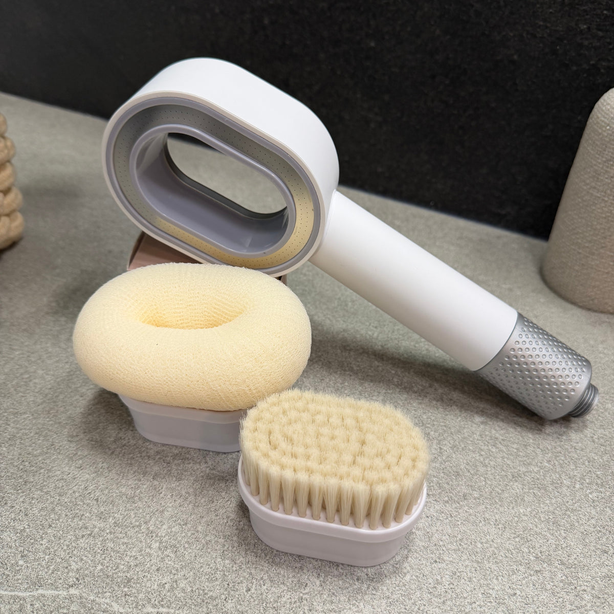 Pommeau de douche filtrant EOVAA blanc et argenté, accompagné d’une brosse exfoliante et d’une éponge de douche sur un support gris.